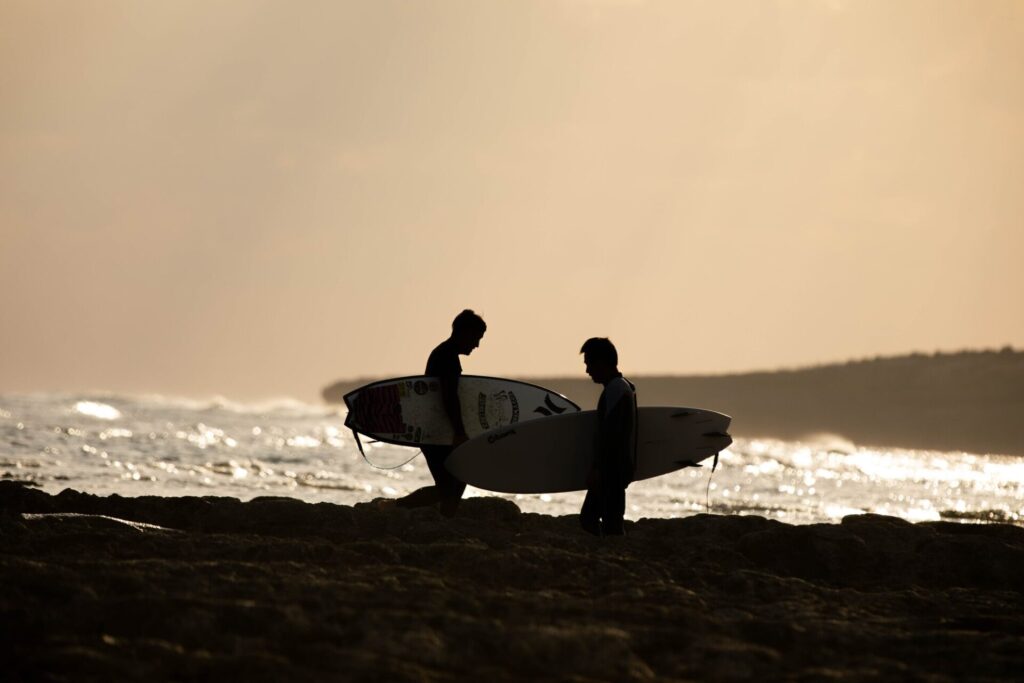 沖縄の夕方の海辺でサーフィンを楽しむ二人組