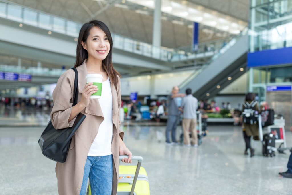 空港内で、コーヒー片手にスーツケースで移動する女性