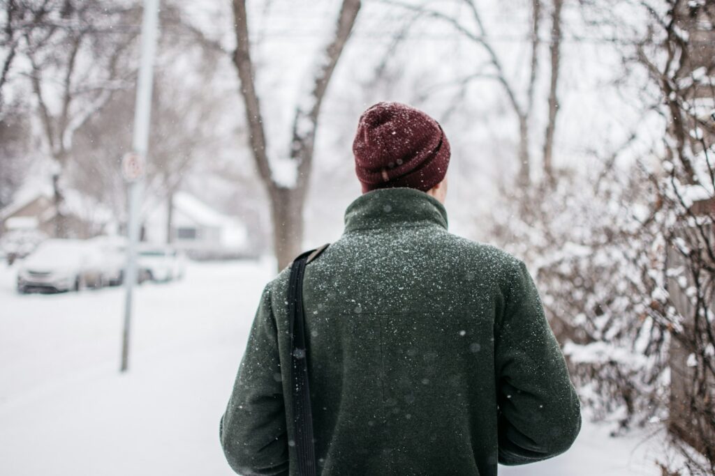 person in red knit cap and green top looking at trees with snow