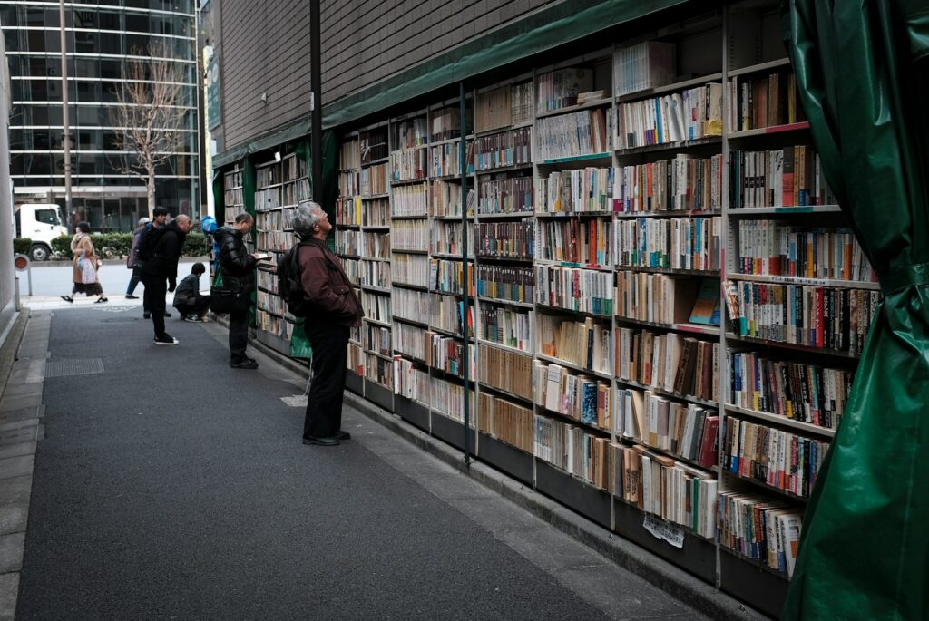 man in black jacket standing near books in book shelves